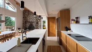 Een moderne keuken met een accentmuur van steen, een centraal eiland, hanglampen en uitzicht op de omgeving.
