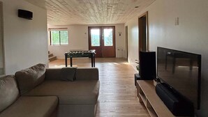 Een woonkamer met een bank, een televisie, een pooltafel en een deur naar een balkon.
