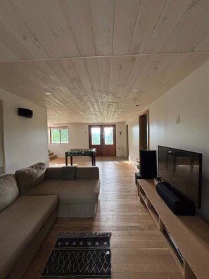 Ein Wohnzimmer mit einer Couch, einem Fernseher, einem Billardtisch und einer Tür, die auf einen Balkon führt.