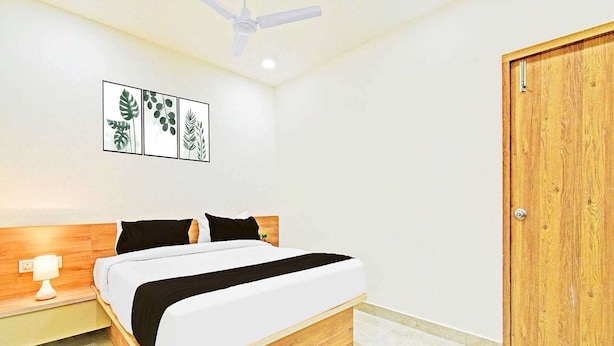 A bedroom with a bed, a nightstand, a ceiling fan, a wooden door, and wall art. - Premium King Bed Room Palette Hotel Amritsar (Amritsar)