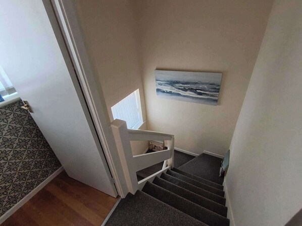 Una escalera con barandilla blanca, escalones alfombrados y un cuadro de una vista marina en la pared.