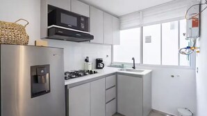 Una cocina moderna con un refrigerador de acero inoxidable, un microondas integrado, una estufa a gas y un lavamanos.