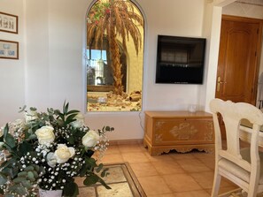 A room with a large window, a wooden cabinet, a white chair, and a TV mounted on the wall. - 4 Bedroom luxury Villa with Pool (AN)