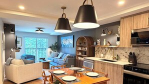 A modern kitchen with a built-in oven, a dining area with a wooden table and chairs, and a living area with a sofa and a coffee table.