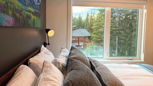 A bedroom with a large window, a painting on the wall, and a lamp.