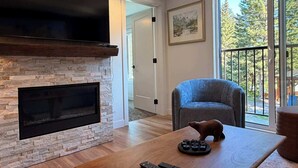 A living room with a stone fireplace, a mounted TV, a blue armchair, a wooden coffee table, and a bear figurine.