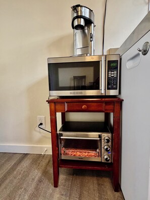 Een keuken met een magnetron, broodrooster en koffiezetapparaat op een houten standaard.