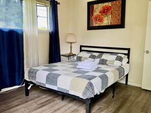 Een netjes opgemaakt bed met een geruit sprei, een lamp op een nachtkastje en een ingelijst foto aan de muur.