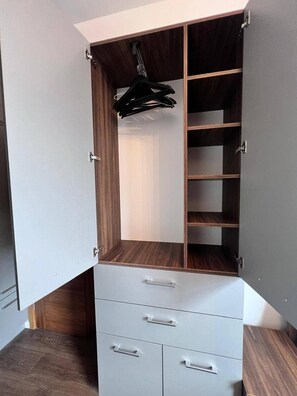 A walk-in closet with open doors, wooden shelves, and a hanging rack.