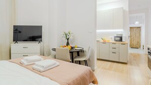 Ett hotellrum med en säng, en TV, ett matbord med stolar, en liten köksdel och en dörr av trä.