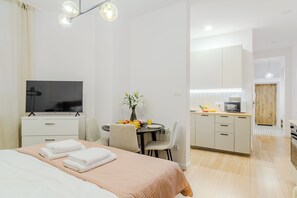 A hotel room with a bed, a TV, a dining table with chairs, a kitchen area, and a wooden door. - Cozy City Center Apartment in Warszawa (Warsaw)