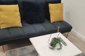 Ein dunkelgraues Sofa mit zwei gelben Kissen und einem weißen Couchtisch mit Pflanze und Fernbedienung.