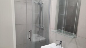 Un bagno moderno con cabina doccia in vetro, ripiano in vetro e lavandino bianco.