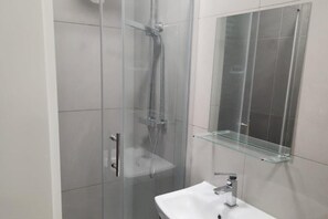 Ein modernes Badezimmer mit Duschkabine aus Glas, einer Glasablage und einem weißen Waschbecken.