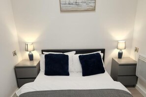 Ein ordentlich bezogenes Bett mit zwei Kissen, zwei Nachttischen mit Lampen und einem Bild an der Wand.