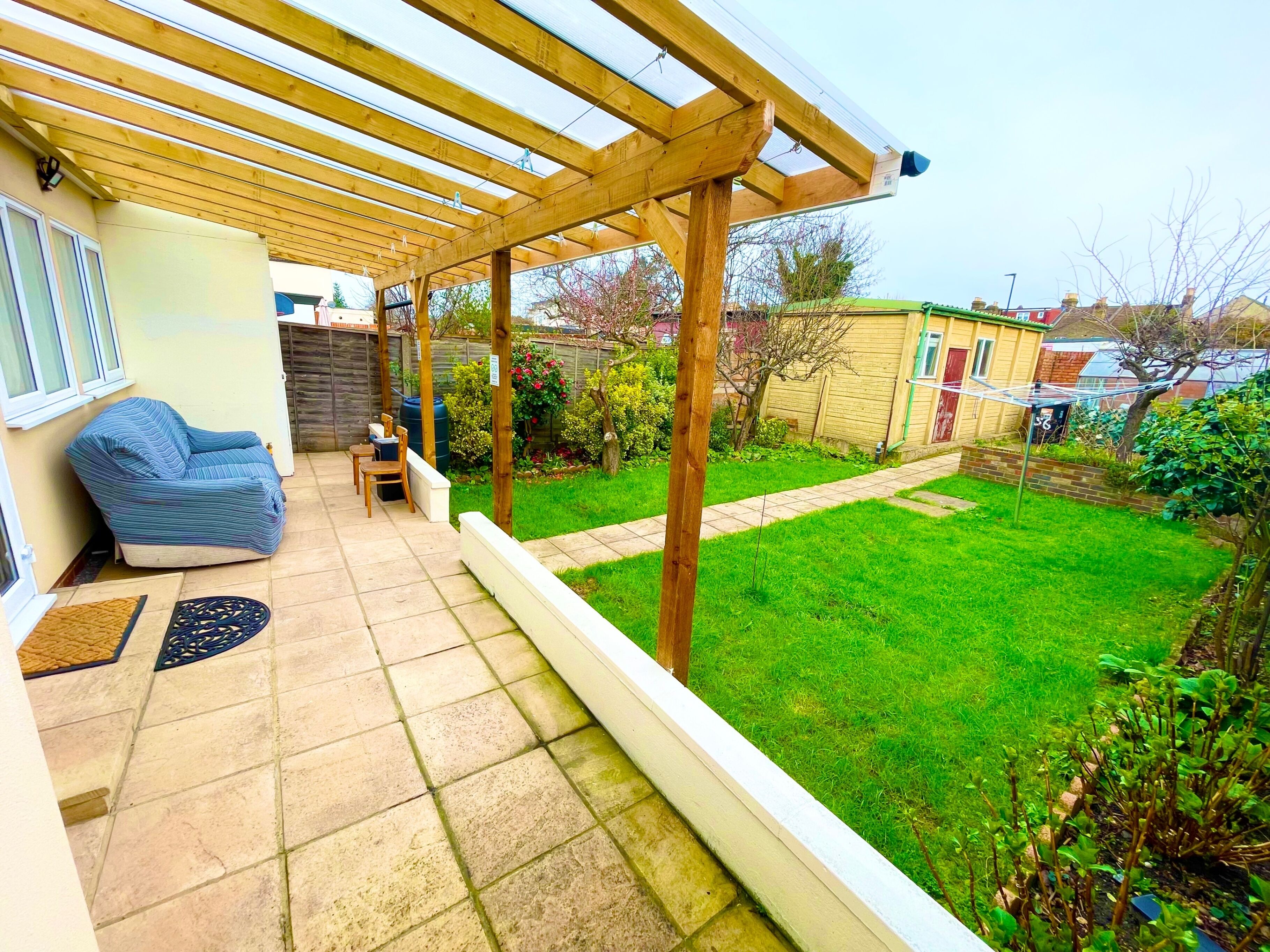 A covered patio with a wooden pergola, a blue sofa, a small table, and chairs.