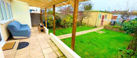 A covered patio with a wooden pergola, a blue sofa, a small table, and chairs.