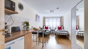 A compact room with a kitchenette, a dining area, two single beds, a large mirror, and a window with curtains. - Cozy Twin bed Studio- North London- Free Parking (Enfield)