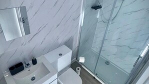 Um banheiro moderno com parede de mármore, pia branca, vaso sanitário e box de vidro.