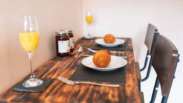 A wooden table with two plates of croissants, a glass of orange juice, and a jar of jam.