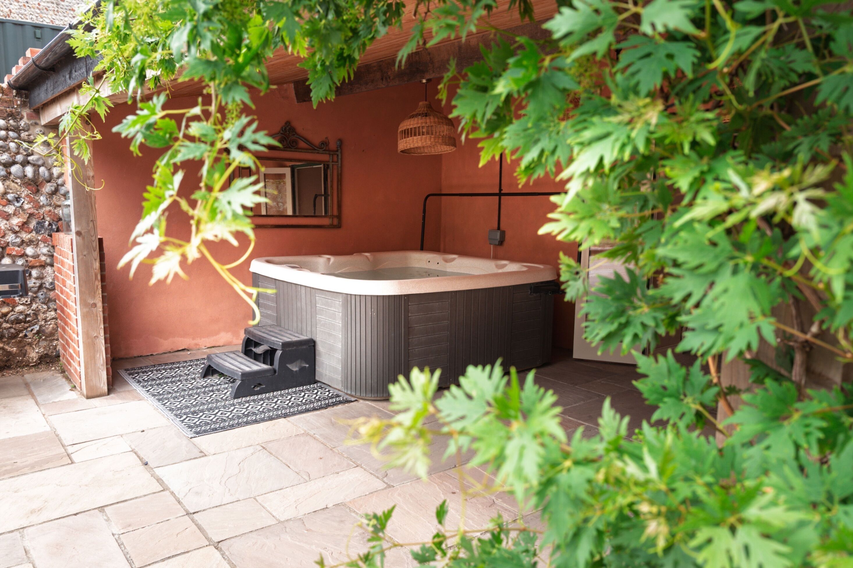 A hot tub in a covered outdoor area with a stone wall, a wooden bench, and a patterned rug.