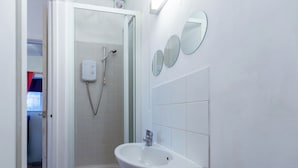 Un baño con ducha, lavamanos y tres espejos colocados en la pared.