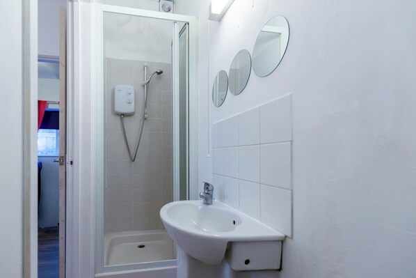 Une salle de bain équipée d’une douche, d’un lavabo et de trois miroirs fixés au mur.