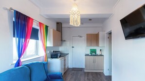 Un espacio habitable compacto con kitchenette, un sofá y un televisor montado en la pared.