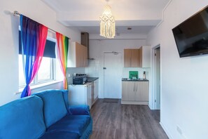 Ein kompakter Wohnbereich mit Küchenzeile, einer Couch und einem an der Wand befestigten Fernseher.