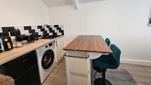 Eine kleine Küche mit Waschmaschine, Kaffeemaschine und Spüle mit schwarz-weißer Rückwand.