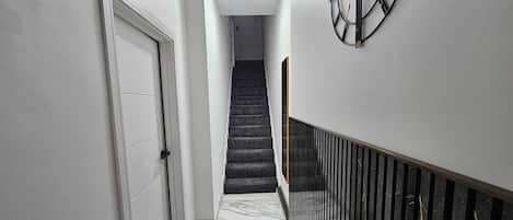 A hallway with a marble floor, a staircase, and a wall-mounted clock.