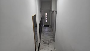 Ein schmaler Korridor mit weißen Wänden und einem Marmorboden. Am Ende des Ganges ist eine Tür mit dekorativer Glasverkleidung zu sehen.