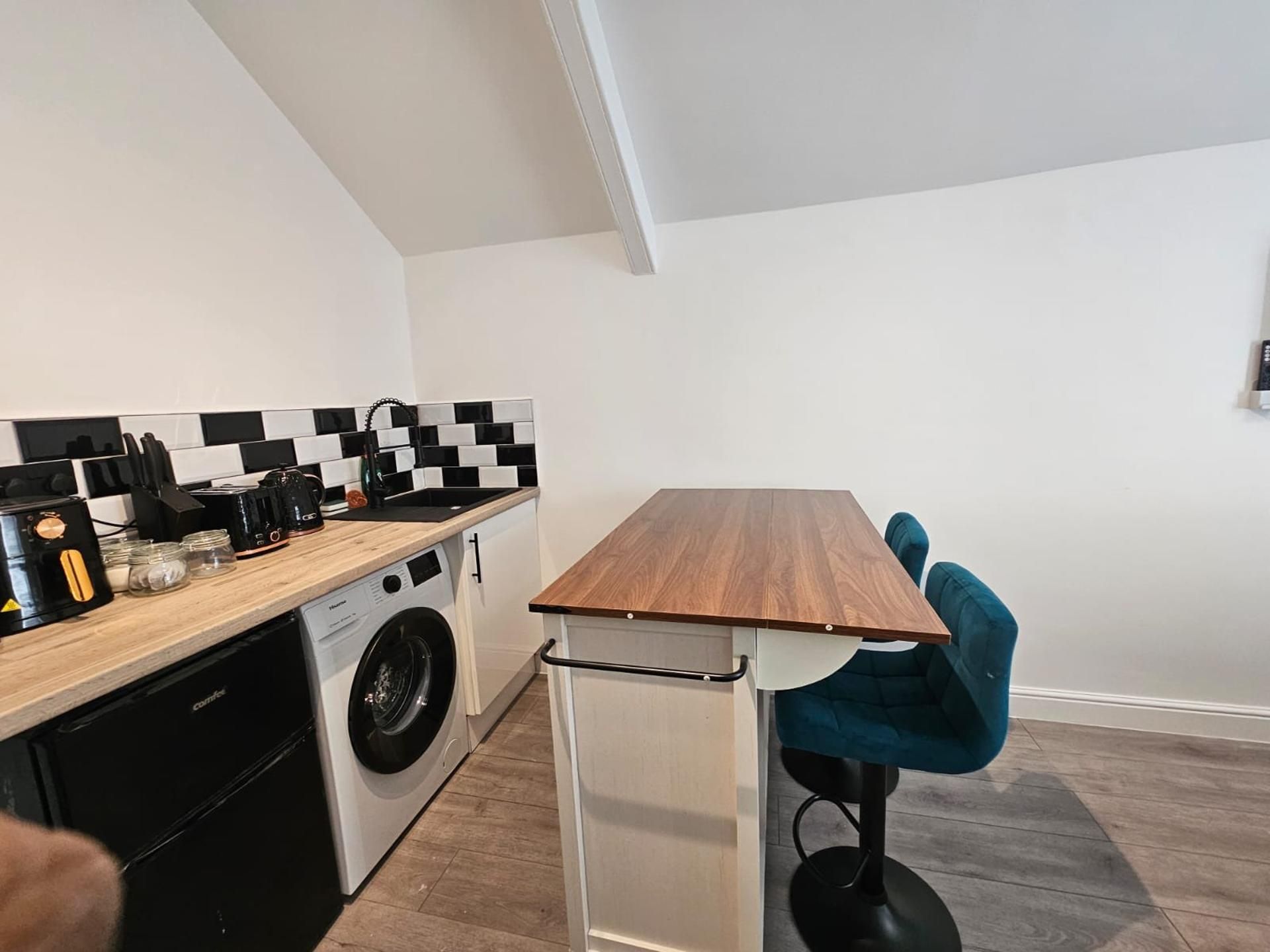 A compact kitchen with a washing machine, a coffee maker, and a checkered backsplash.
