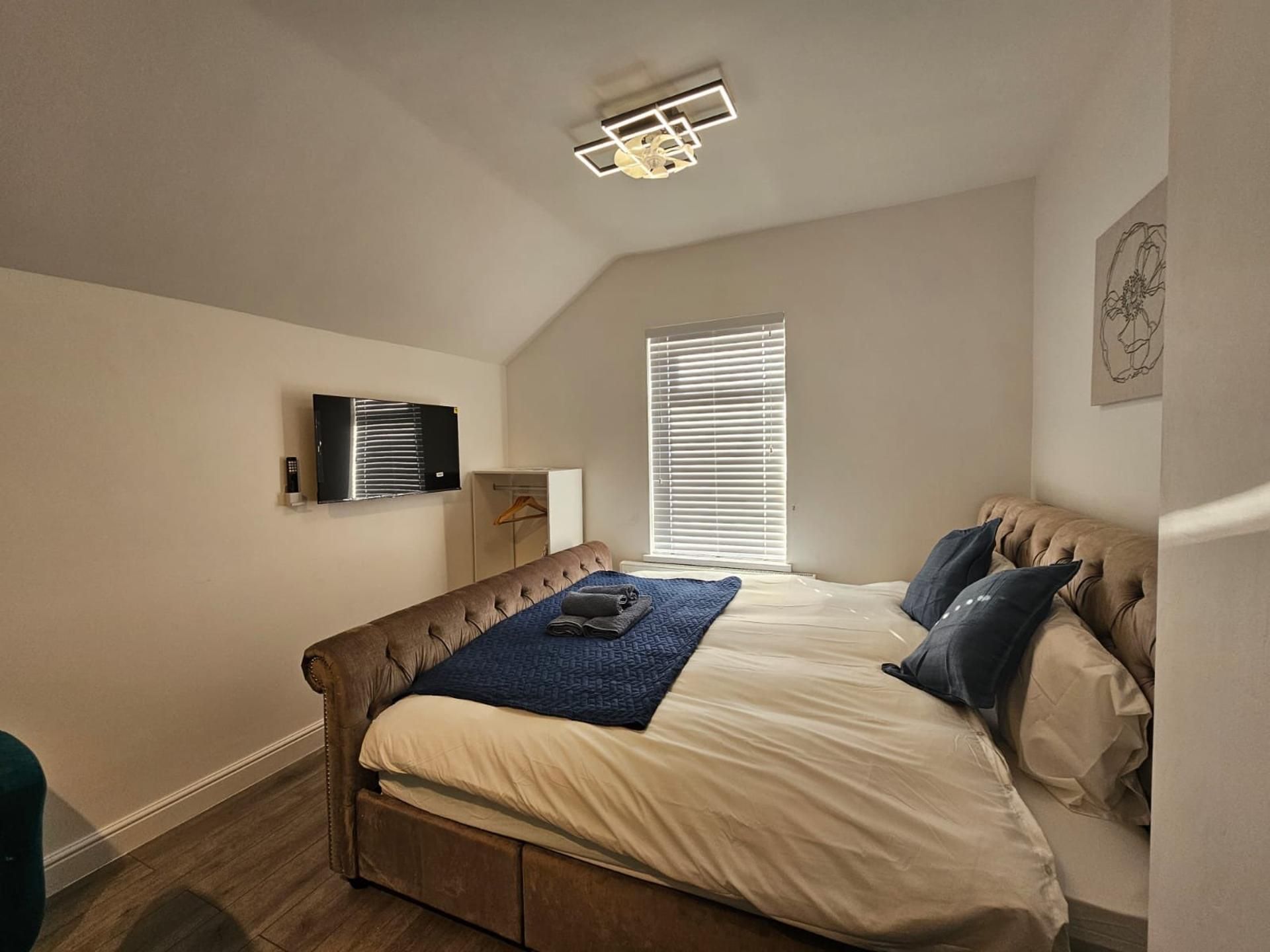 A bedroom with a bed, a ceiling fan, a window with blinds, and a wall-mounted air conditioning unit.