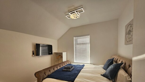 Ein Schlafzimmer mit Bett, Kleiderschrank, Fernseher und einem Fenster mit Jalousien.