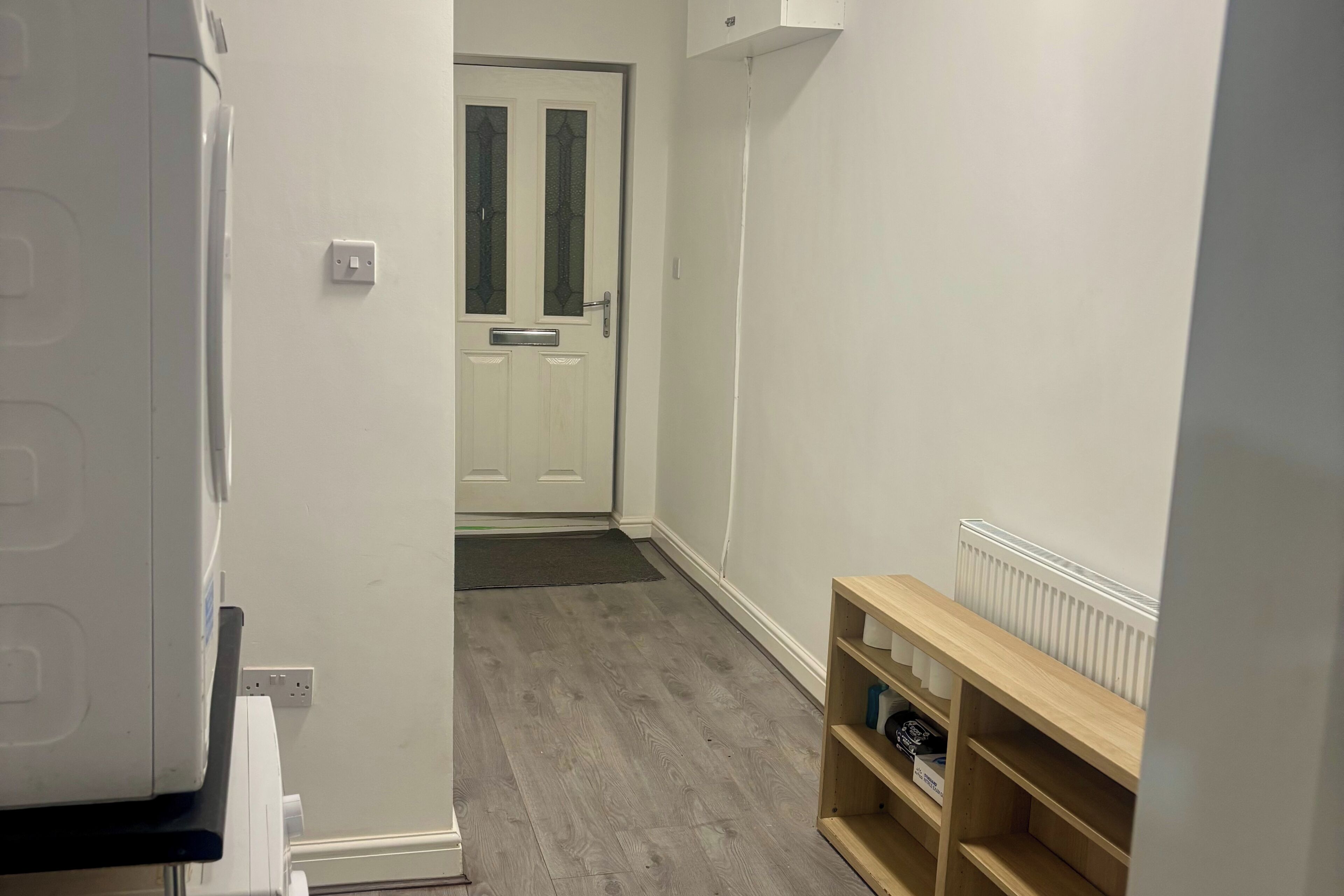 A hallway with a white door, a radiator, and a wooden shelf.