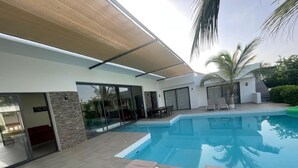 A modern outdoor pool area with lounge chairs, a dining table, and a covered patio.