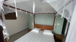 A single bed with a wooden headboard, two bedside tables, and a mosquito net.