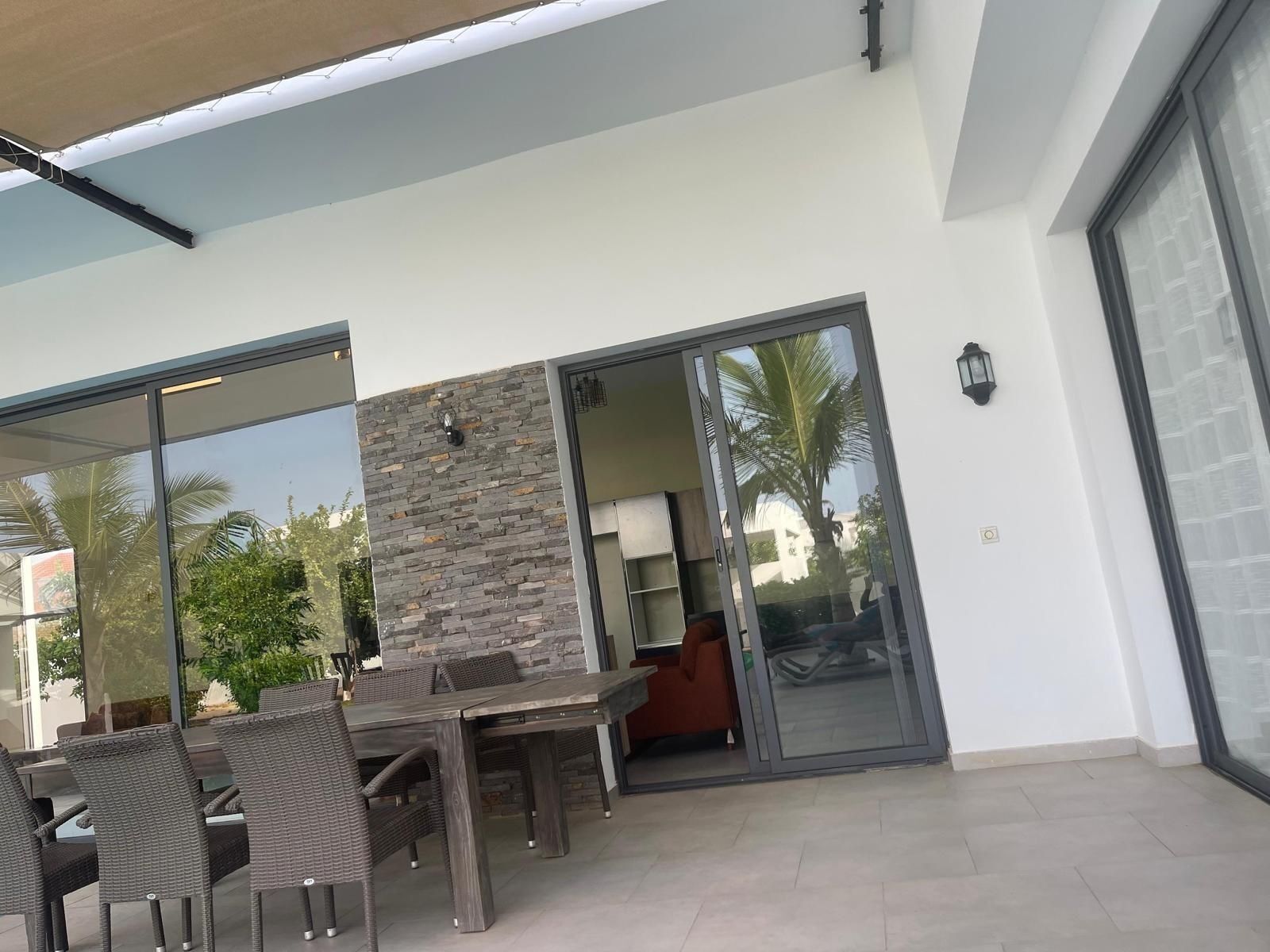 An outdoor dining area with a table and chairs, a stone wall, and a sliding glass door leading to a covered patio.
