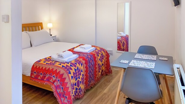 Ett hotellrum med en säng, ett skrivbord, en stol, en spegel och en taklampa.