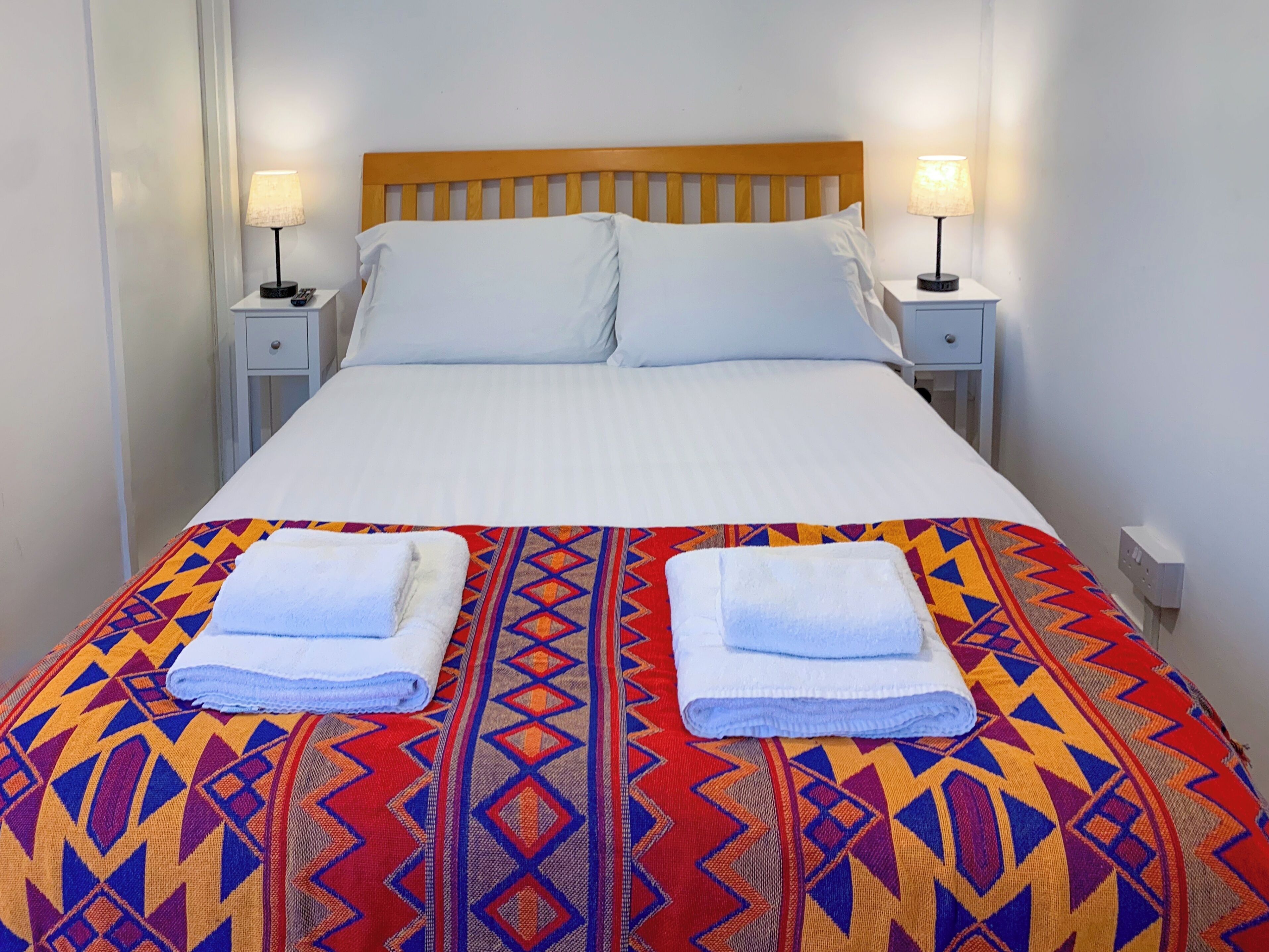 Un lit double avec une couvre-lit à motifs, deux oreillers blancs, deux tables de chevet avec des lampes et deux serviettes pliées posées sur le lit.