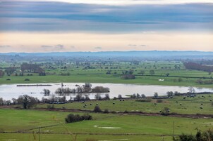 Paisaje rural con campos, un río y colinas lejanas.