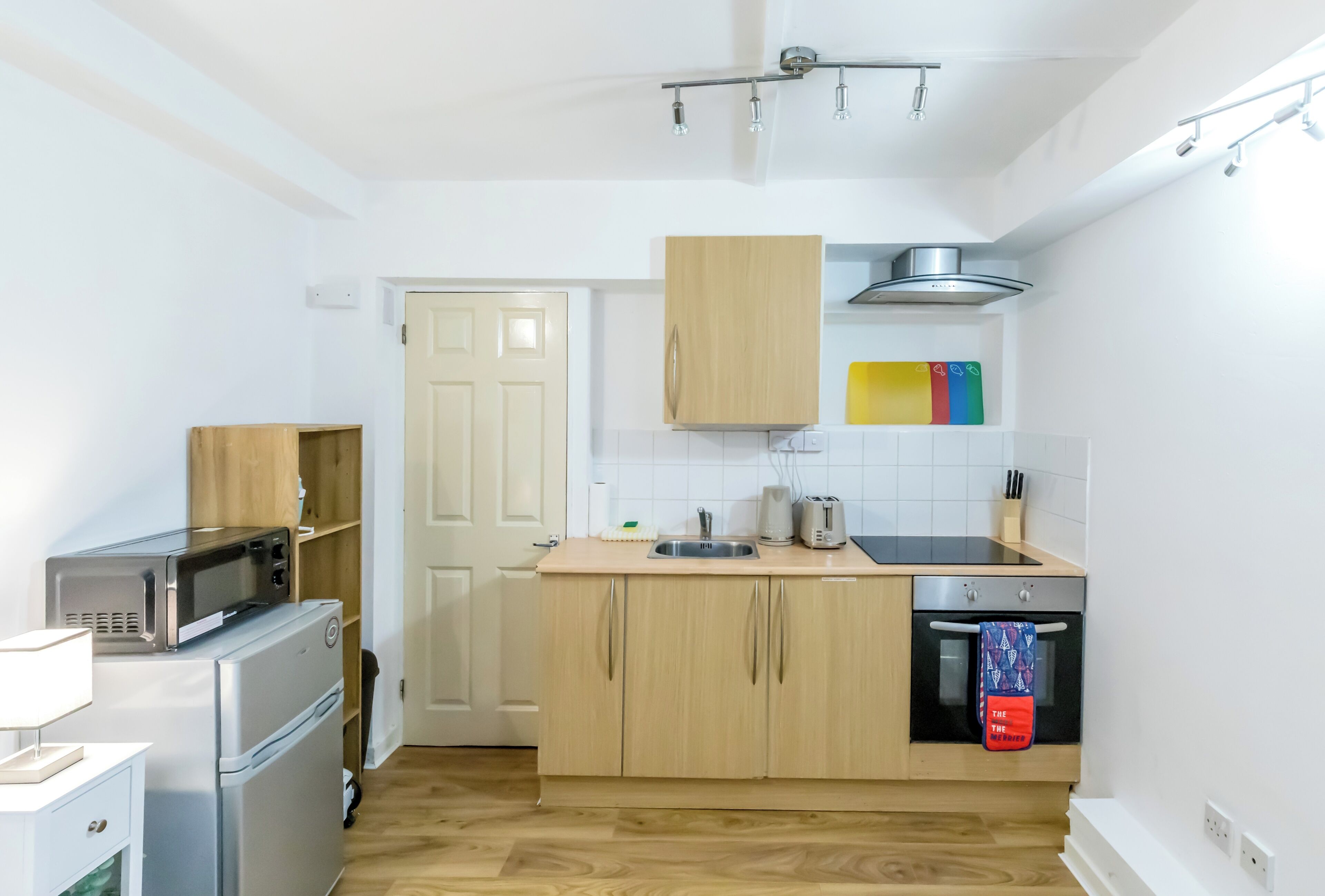 A compact kitchen with a microwave, toaster, and oven, wooden cabinets, and a tiled backsplash.
