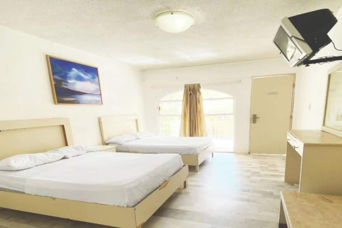 Habitación de hotel con dos camas, un escritorio, una silla, un televisor y una puerta que da a un área exterior.