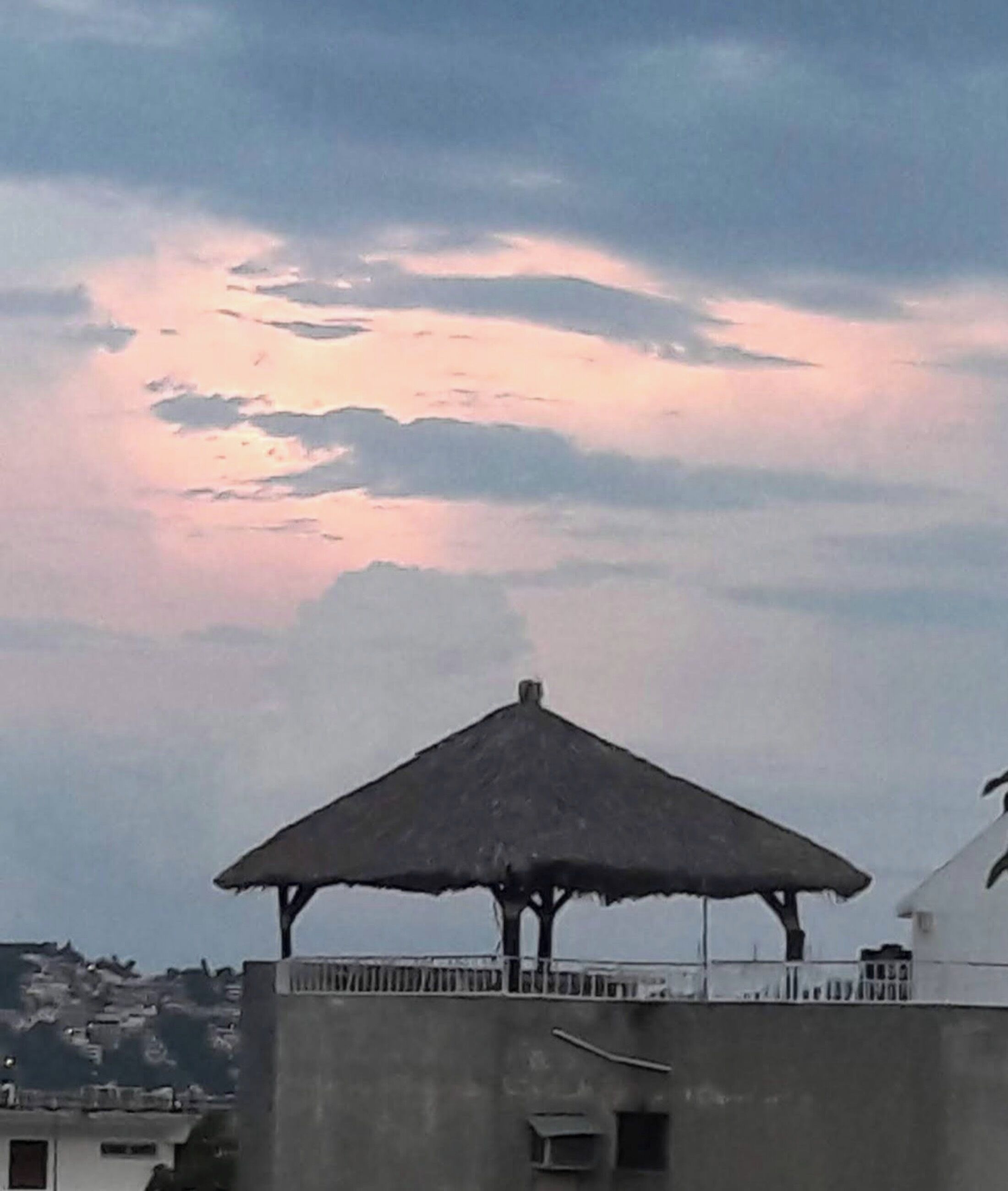 Una estructura con techo de paja en la azotea, posiblemente un pabellón o mirador, con vistas a un cielo nublado.