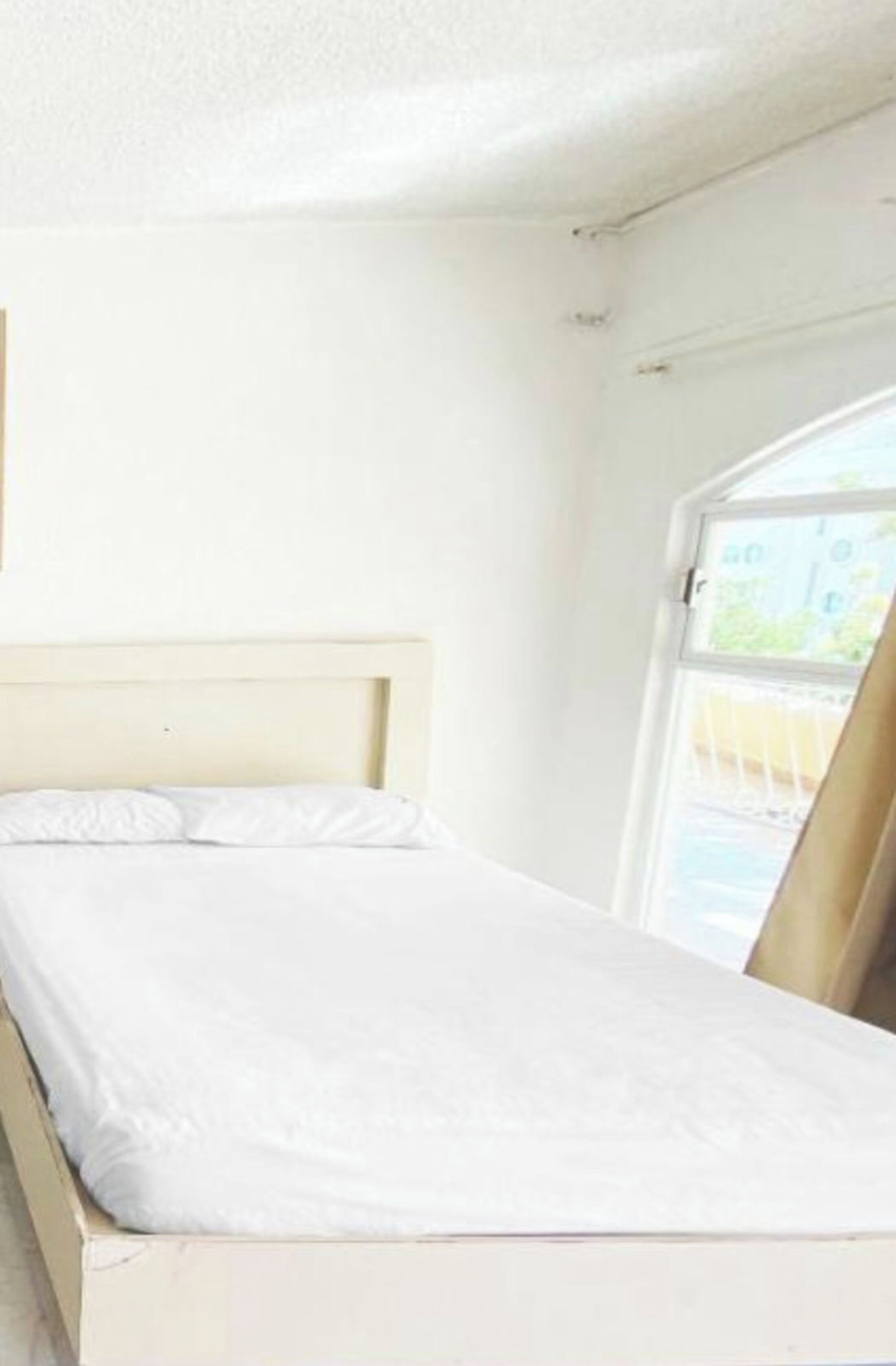 A single bed with a wooden headboard in a room with white walls and a window.