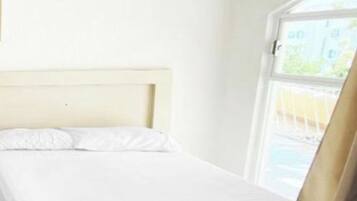 Ein Einzelbett mit Holz-Kopfteil in einem Zimmer mit weißen Wänden und einem Fenster.
