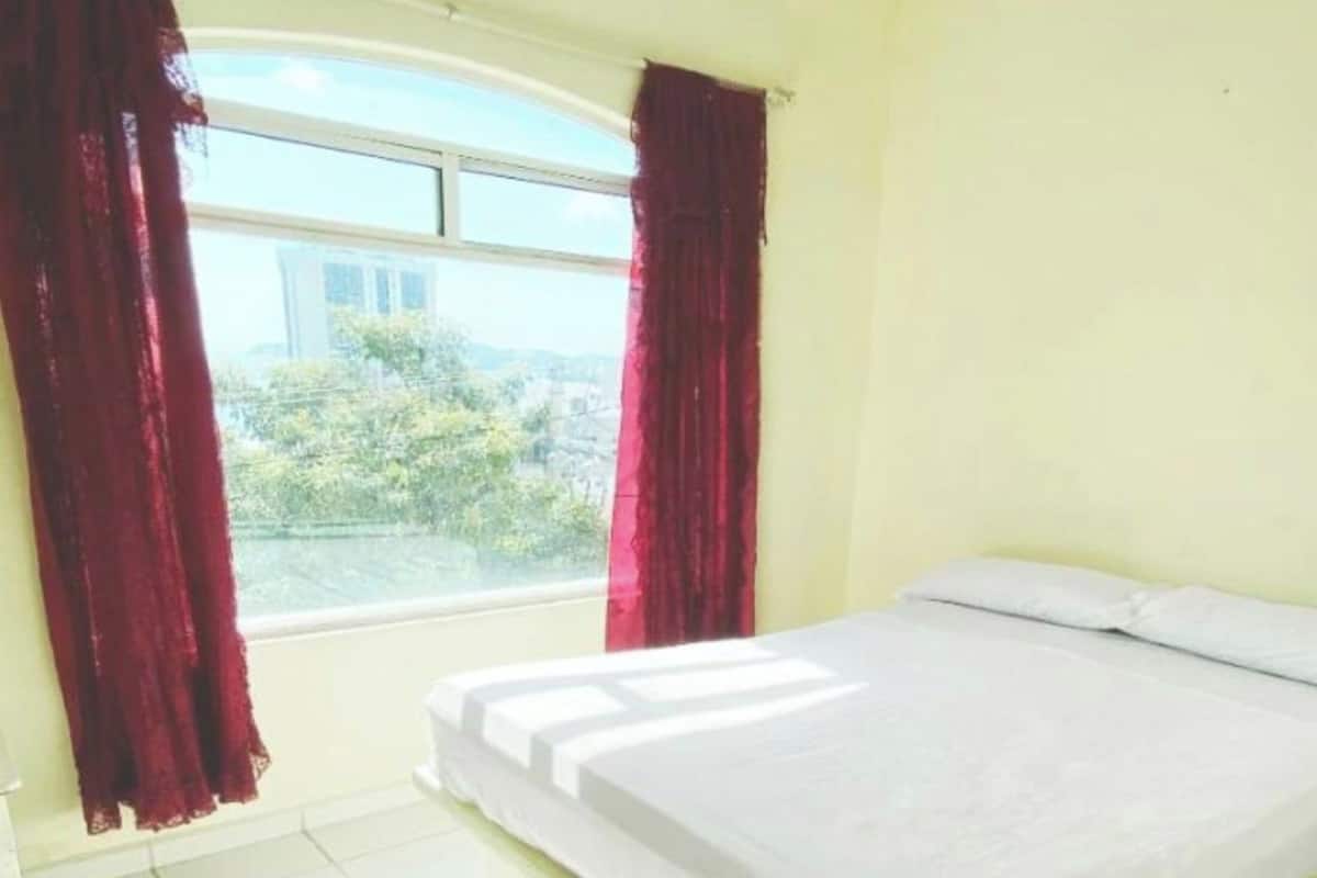 Un dormitorio con cama, ventana con cortinas y vista a la vegetación.
