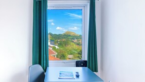 Une pièce comprenant une table et deux chaises, une fenêtre donnant sur un paysage vallonné, ainsi qu’une petite table sur laquelle se trouvent une télécommande et un livret.