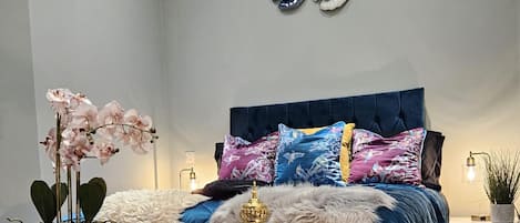A bedroom with a bed, decorative pillows, a nightstand, a lamp, and wall art.